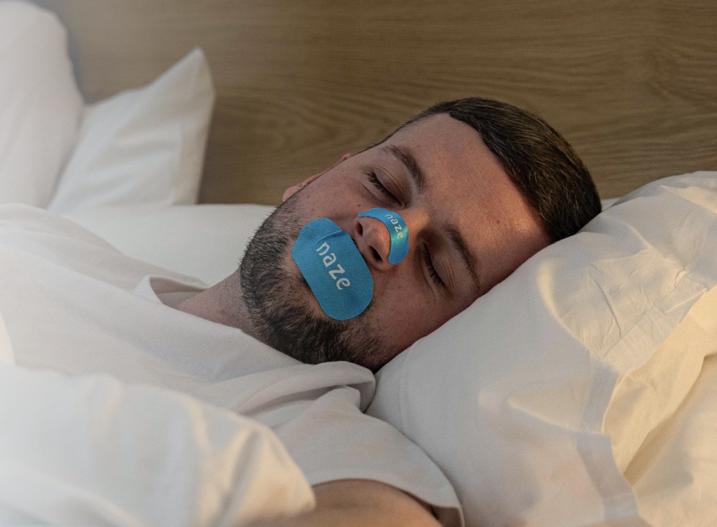 Man asleep wearing Naze mouth tape and a Naze nose strip